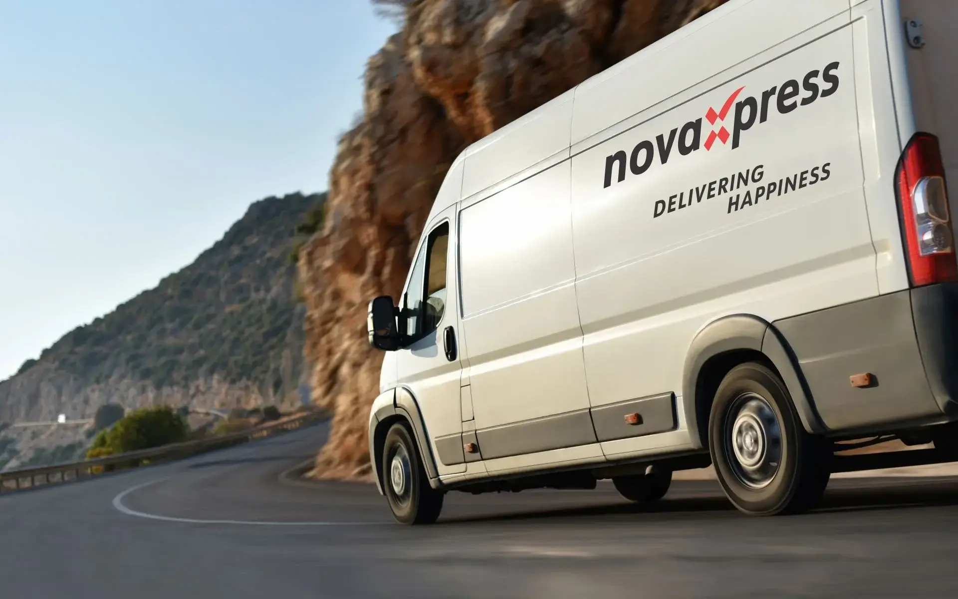 White courier van driving down winding mountain road.